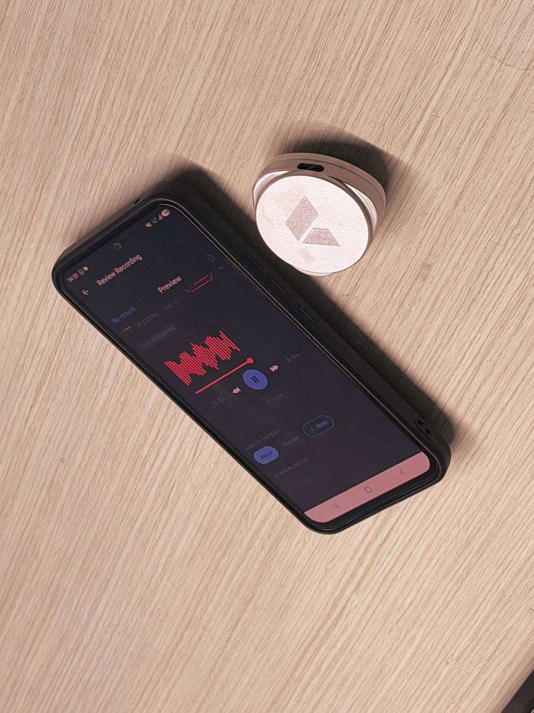 A Plazma auscultation device on a desk beside a smartphone showing a live respiratory waveform in the app.