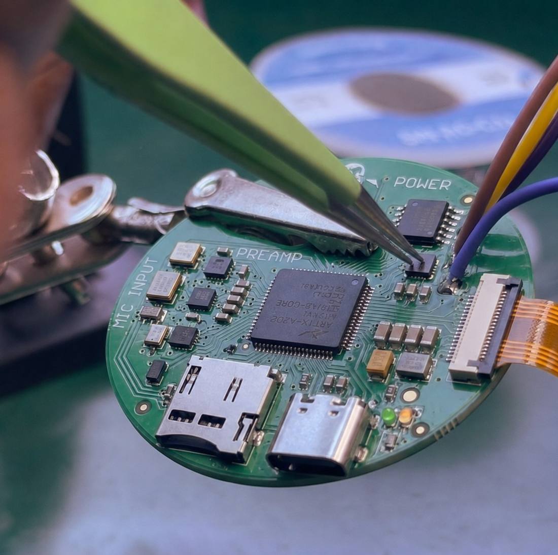 A hand soldering a component onto the round Plazma sensor board, its MIC INPUT, PREAMP and POWER sections labelled on the silkscreen.